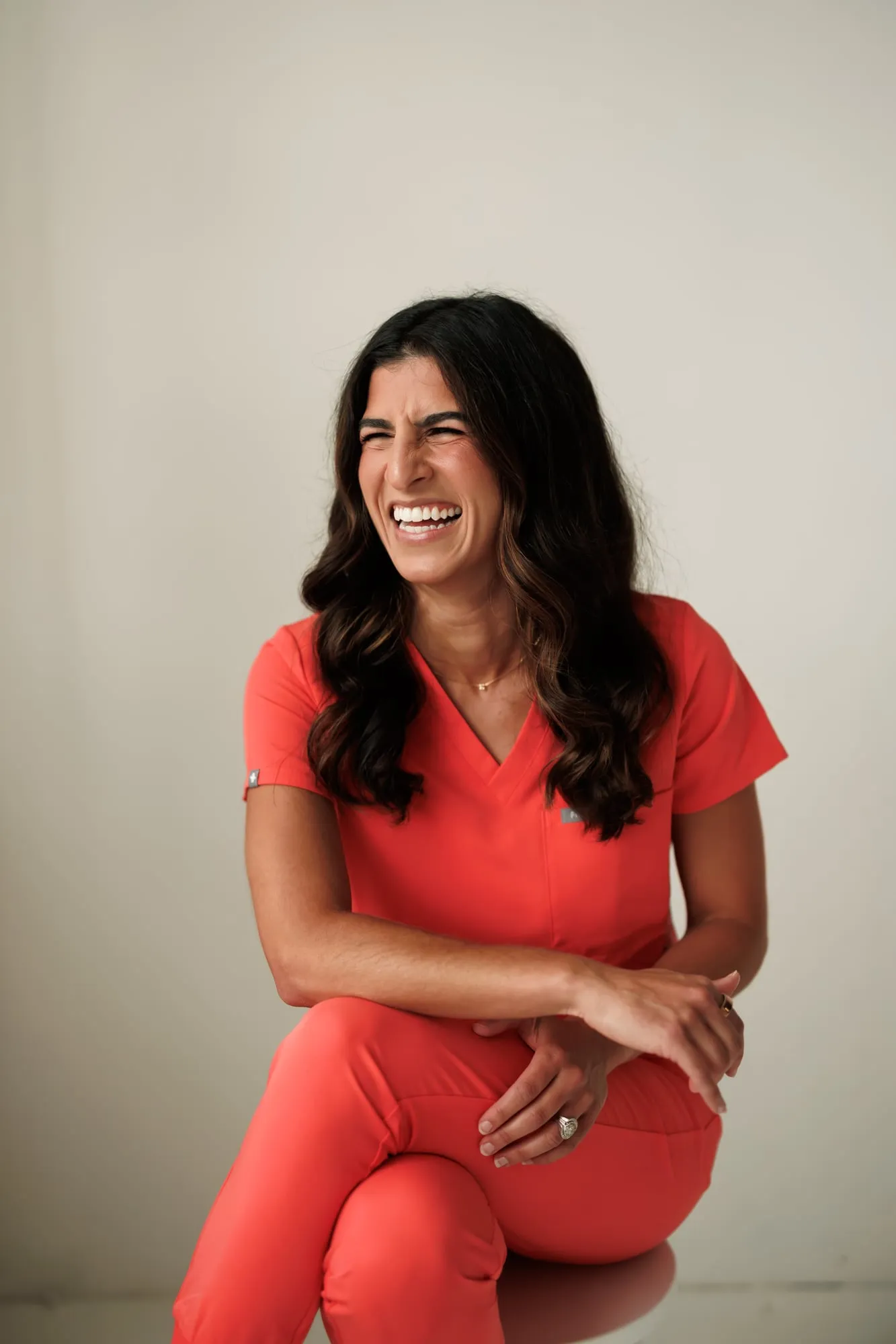 Dr. Caris Miller laughing, seated in coral scrubs