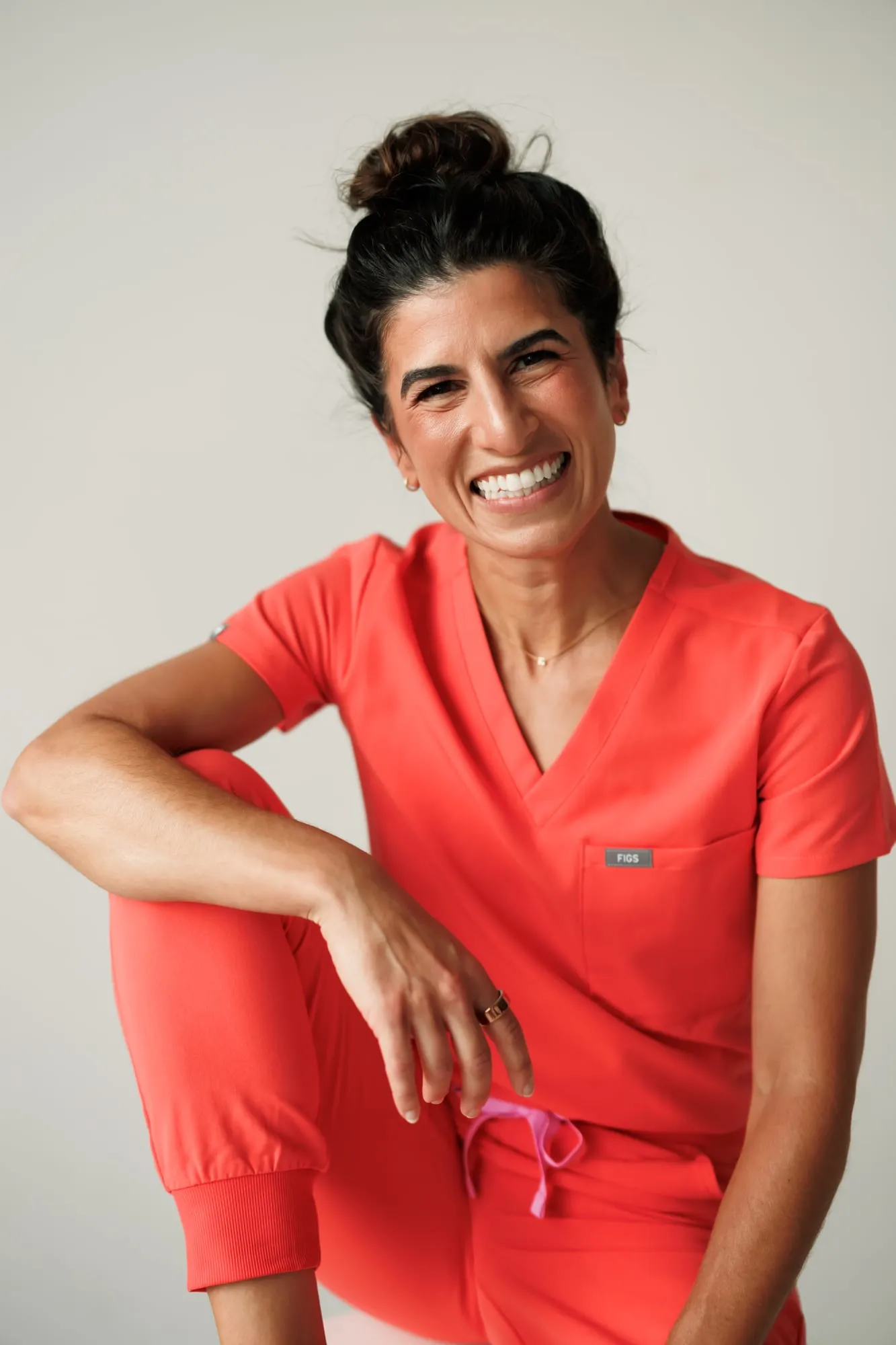 Dr. Caris Miller in coral scrubs, smiling with her arm resting on her knee